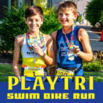 Play Tri Swim Bike Run logo infront of 2 little boys holding medals outside.